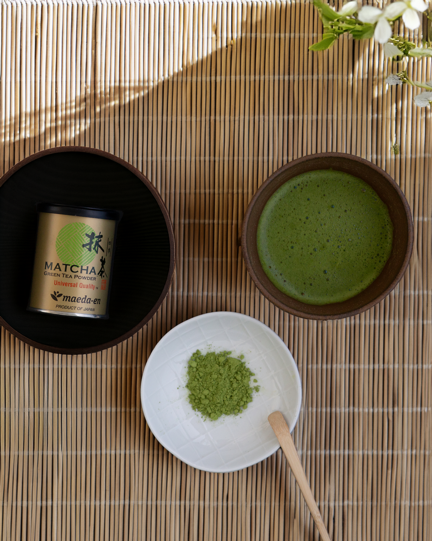 Matcha green tea set with a container, bowl, and whisk on a wooden surface.