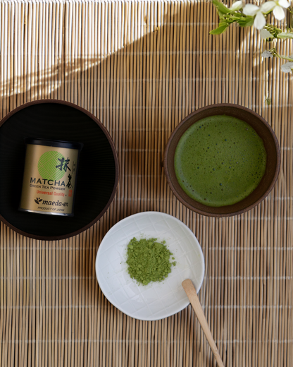 Matcha green tea set with a container, bowl, and whisk on a wooden surface.