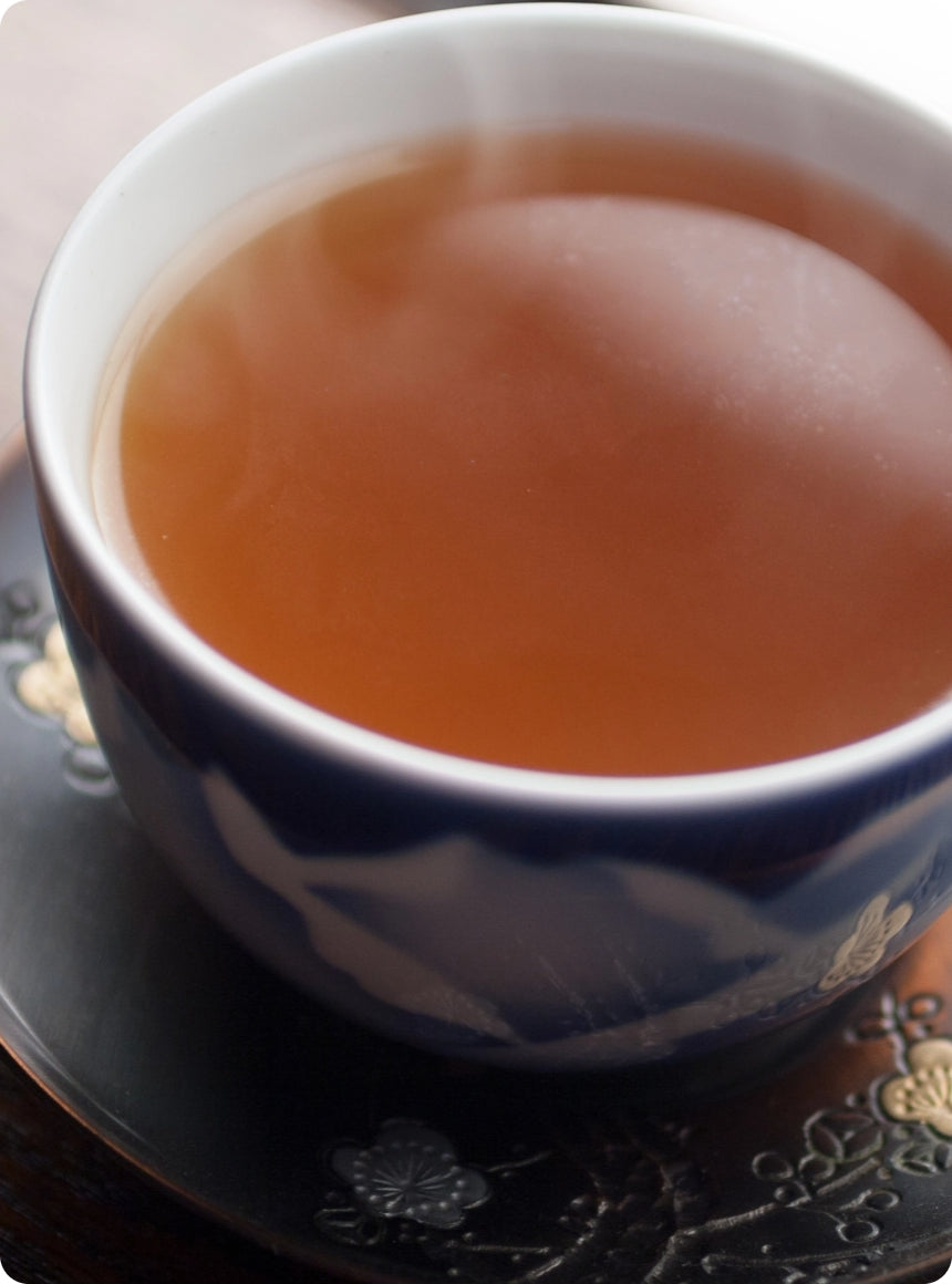 A close-up of a blue and white ceramic teacup filled with amber-brown tea, resting on a dark decorative saucer.